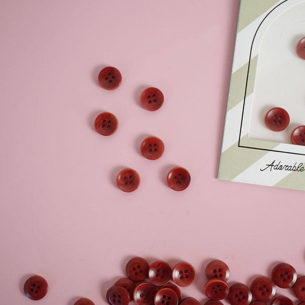 Red buttons scattered on a pink surface with a card labeled 'Adorable' in the corner.
