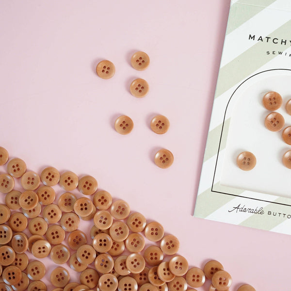 Brown buttons scattered on a pink surface with a 'Matchesfashion' card in the background.