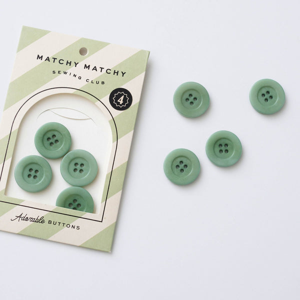 Green buttons with packaging labeled 'Matchy Matchy Sewing Club' on a white background