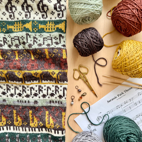 Knitted fabric with pattern, yarn balls, knitting needles, and scissors on a wooden surface.
