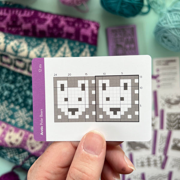 Hand holding a card with a knitting pattern surrounded by yarn and fabric