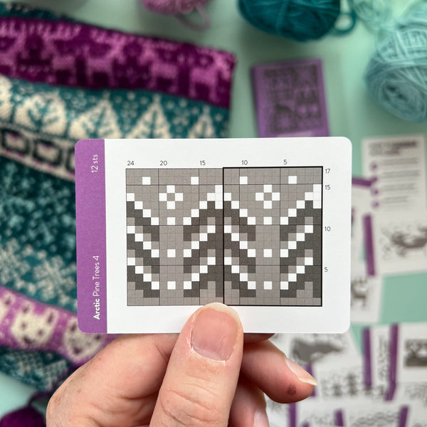 Hand holding a pattern card with yarn and knitting patterns in the background