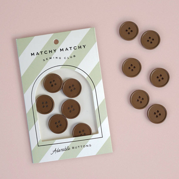 Set of brown buttons with packaging labeled 'Matchy Matchy Sewing Club' on a pink background