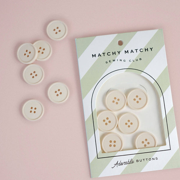 Packaged buttons with a matching set of buttons on a pink background