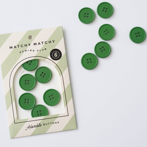 Green buttons with packaging labeled 'Matchy Matchy Sewing Club' on a white background