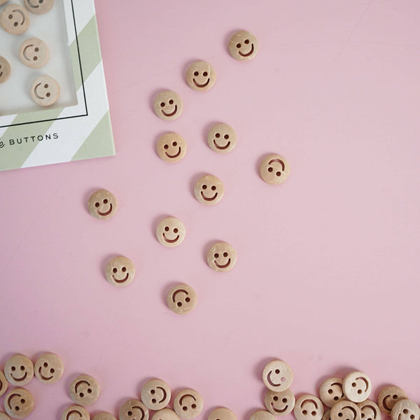 Smiley face buttons scattered on a pink surface with a box of buttons in the corner.