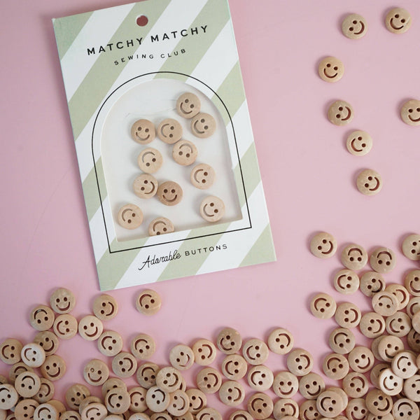 Smiley face buttons with a 'Matchy Matchy Sewing Club' package on a pink background