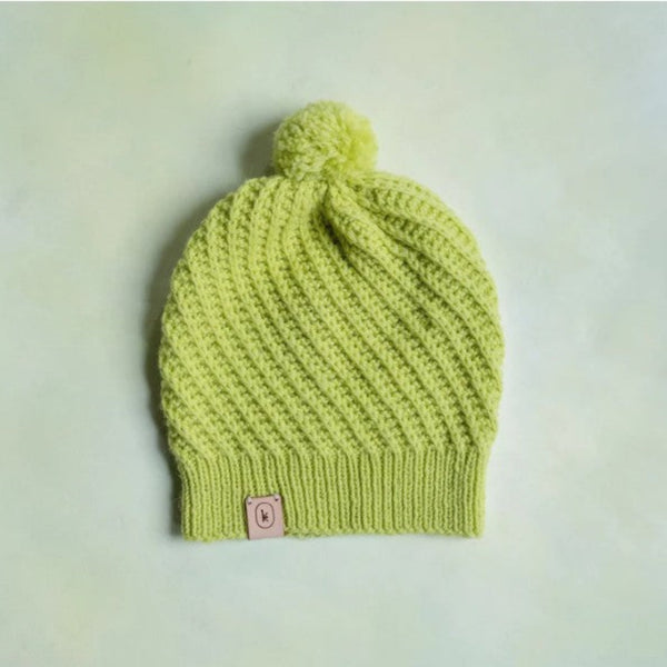 Green knitted beanie with a pom-pom on a light gray background