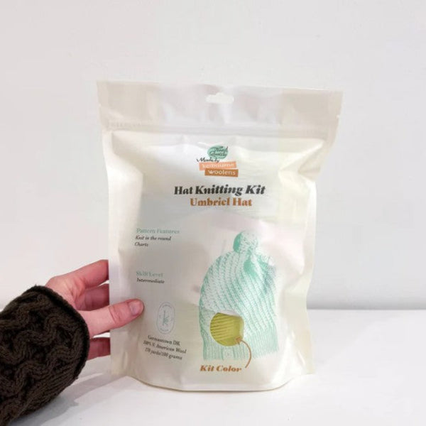 Hand holding a hat knitting kit packaging against a white background