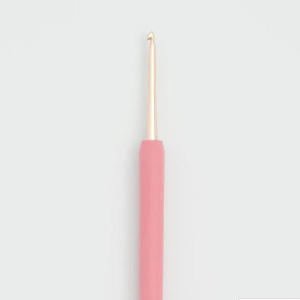 A single crochet hook with a matte pink handle and a metallic gold hook tip, centered against a light gray background.