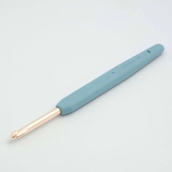 A single crochet hook with a light blue ergonomic handle and a rose gold metal tip, photographed on a clean white background.
