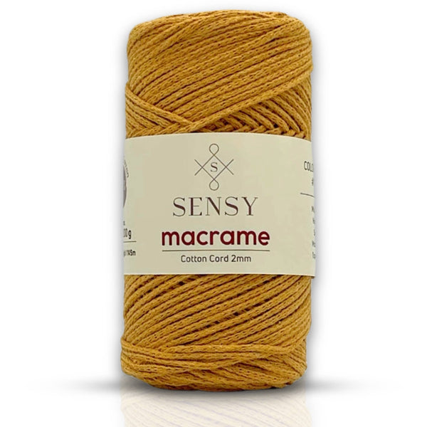 A spool of Sensy Macrame cotton cord in a mustard yellow color, featuring a cream paper label with the brand name and product details.