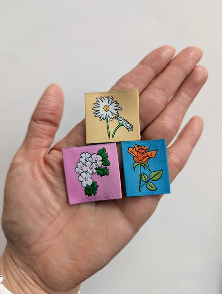 Hand holding three small square art pieces with floral designs on a plain background